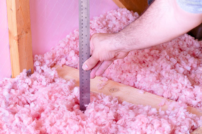 A man measures the height of the insulation in his attic using a ruler.