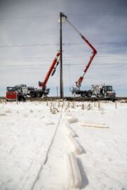 Line crews work to restore power as long tubes of ice that formed on power lines lay on the ground in the foreground of this photo.