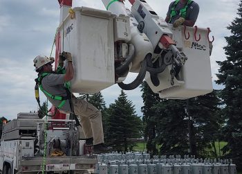A line technician carefully lowers himself to the ground from a bucket.