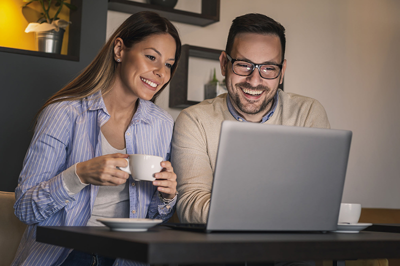A couple looks at their laptop. Todo el portal para clientes, desde inicio de sesión hasta manejo de pagos, notificaciones y más, pronto estará disponible en español.
