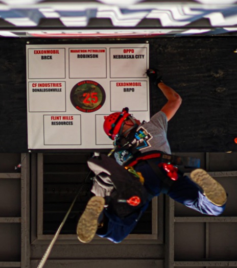 An OPPD team member dangles from a rope as he writes on a sign.