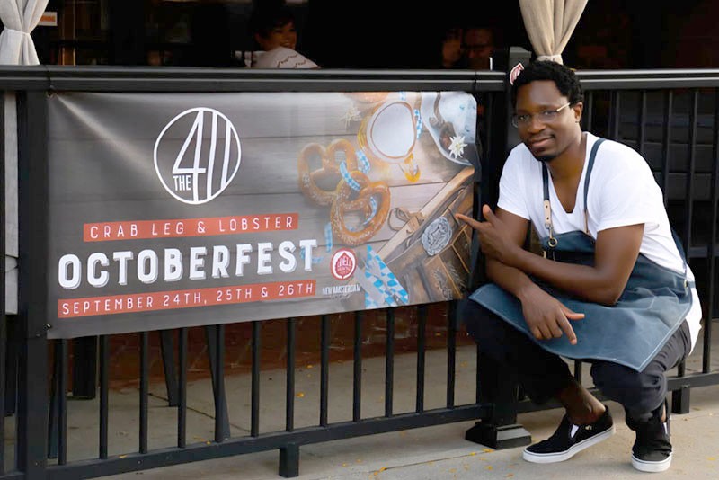 Danny Orwa crouches next to a sign in front of his downtown Norfolk restaurant.