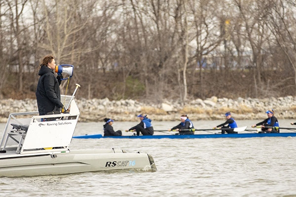 Bridget Navratil holds a megaphone while standing in a separate boat while rowers practice at Carter Lake.