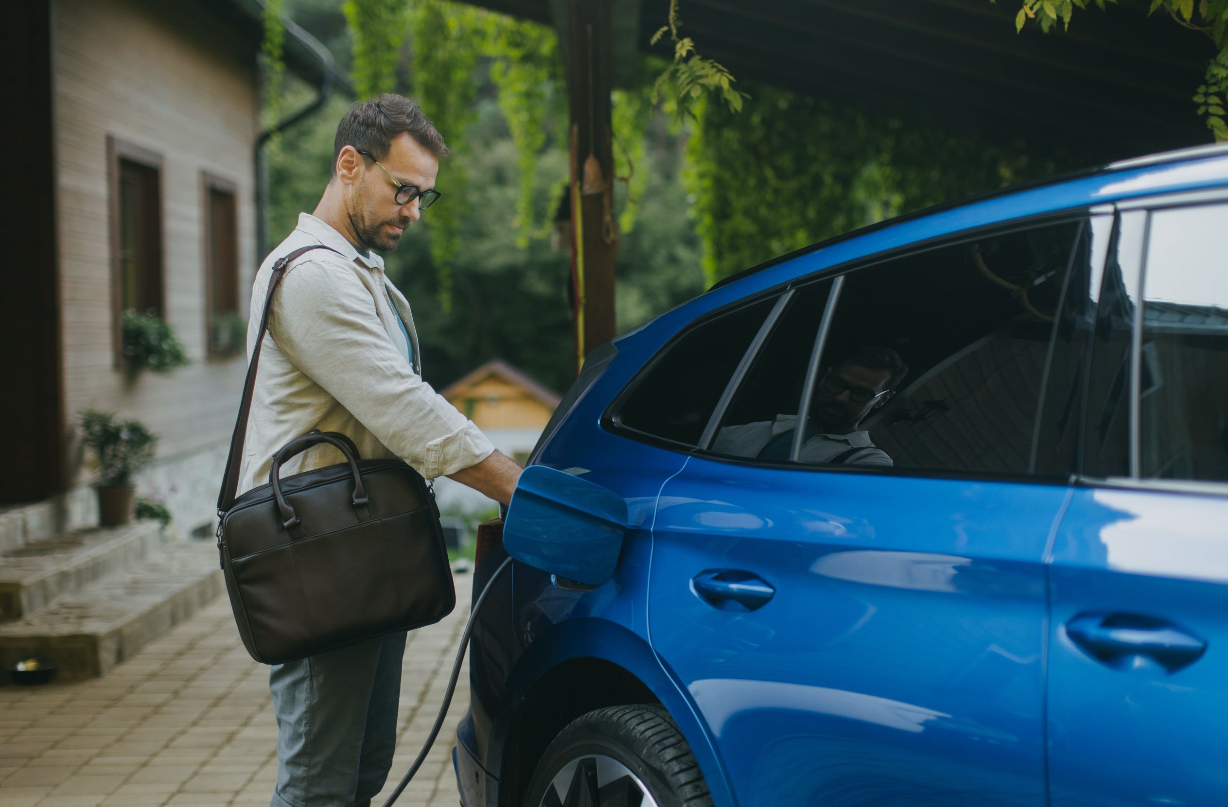 A man charges his electric vehicle outside his home. These tips can help you save money charging your EV and make sure it's always ready to go.