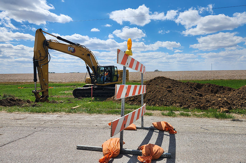 A bulldozer digs below power lines. Long before road workers break ground, OPPD’s utility coordination team works closely with local governments and contractors to identify and relocate infrastructure that’s deemed to be in conflict with road projects, be it poles, padmount transformers or underground power lines. 
