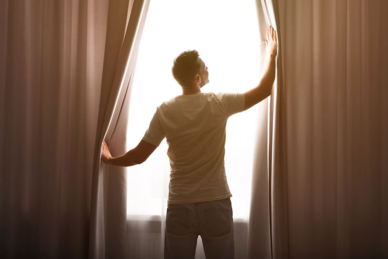 220398513 – man opening window curtains at home, back view