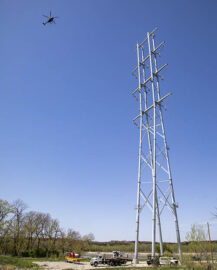 A helicopter moves from one transmission tower to another, stringing a transmission line across the Platte River.